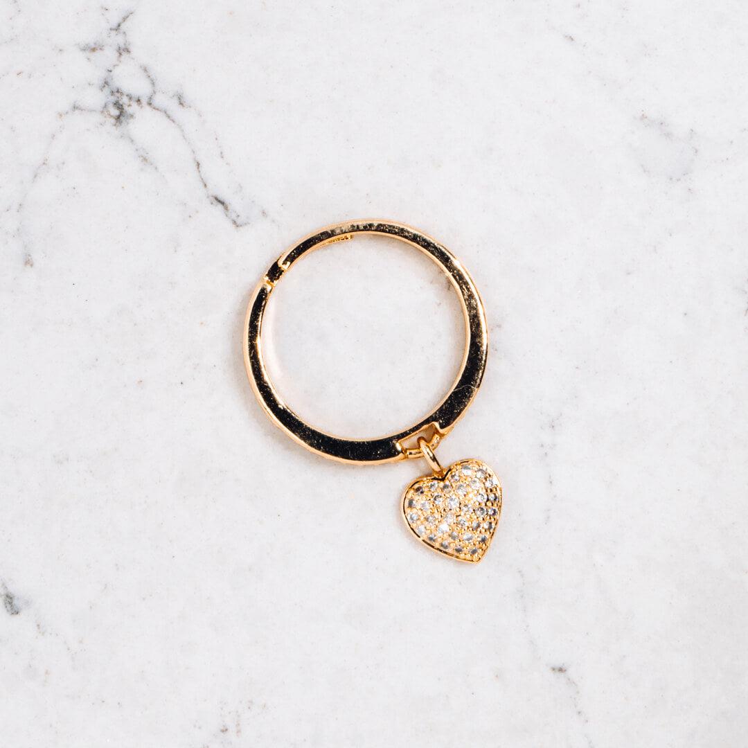 A gold tone and diamante ring with a heart shaped pendant seen from above.