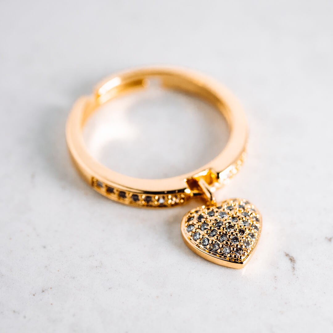 A gold tone and diamante ring with a heart shaped pendant.