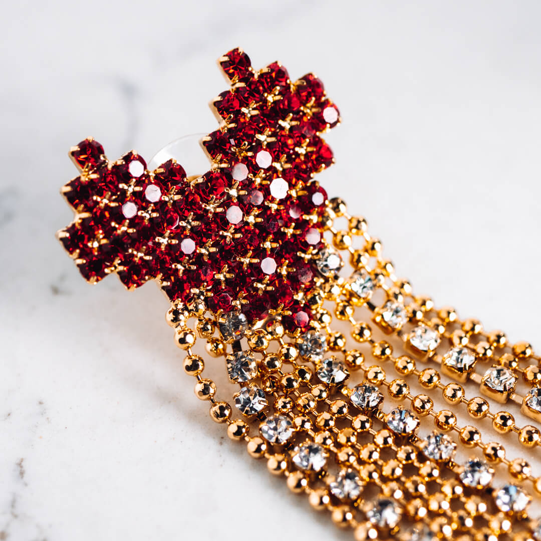 A pair of large earrings made up of a red heart with a gold tone and diamante tail.