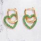 Gold tone earrings with heart shaped pendants in gold tone with emerald green coloured zircon stones.
