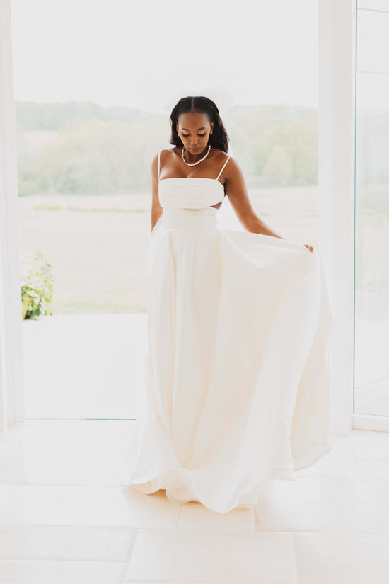 A full length shot of a bride wearing a full-length white wedding dress and a Vellva vegan pearl and bead Il Mare Necklace