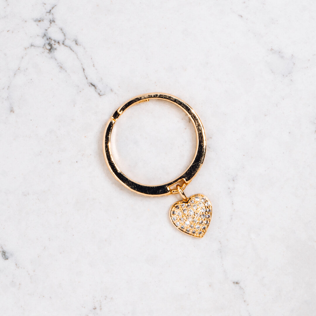 A gold tone and diamante ring with a heart shaped pendant seen from above. 
