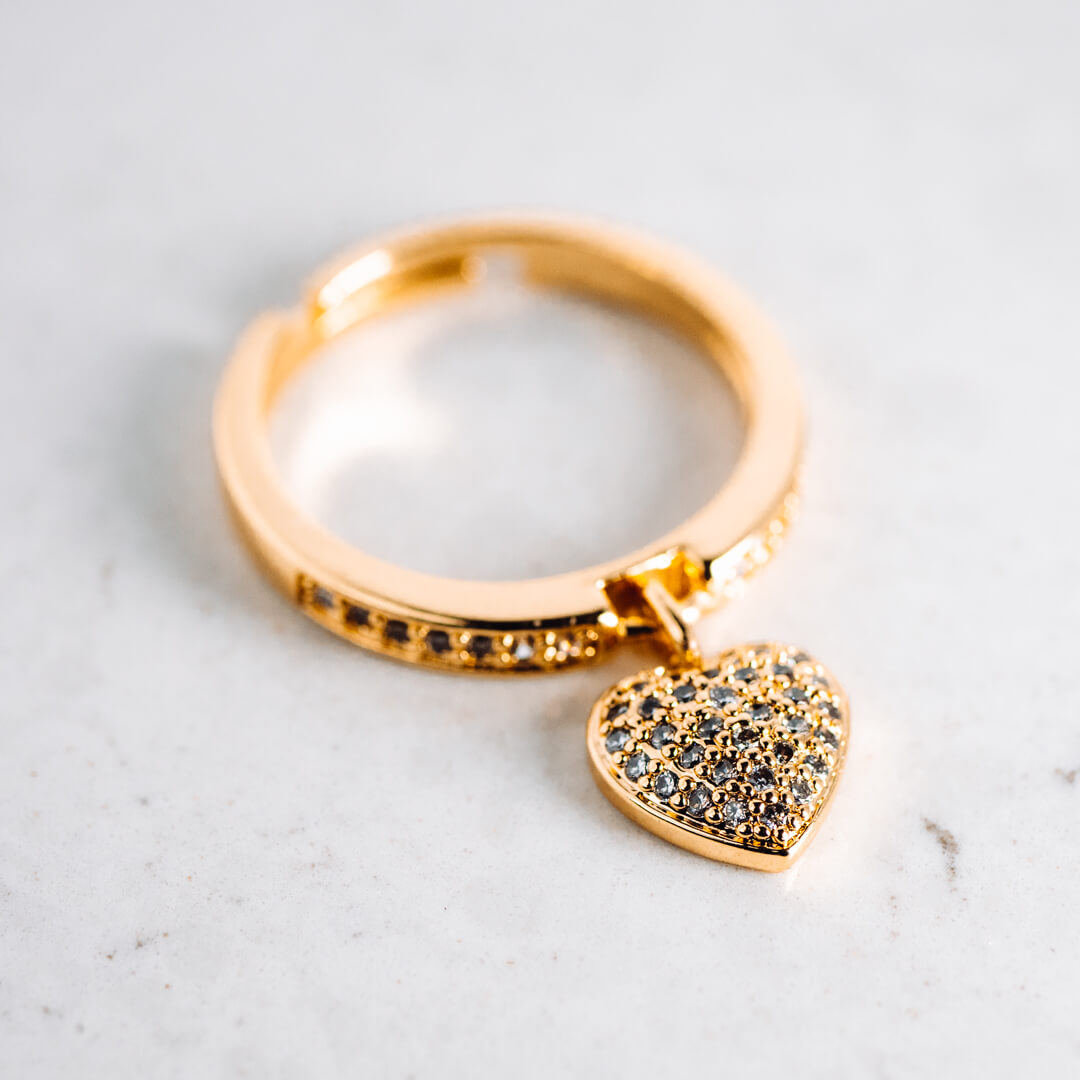 A gold tone and diamante ring with a heart shaped pendant. 
