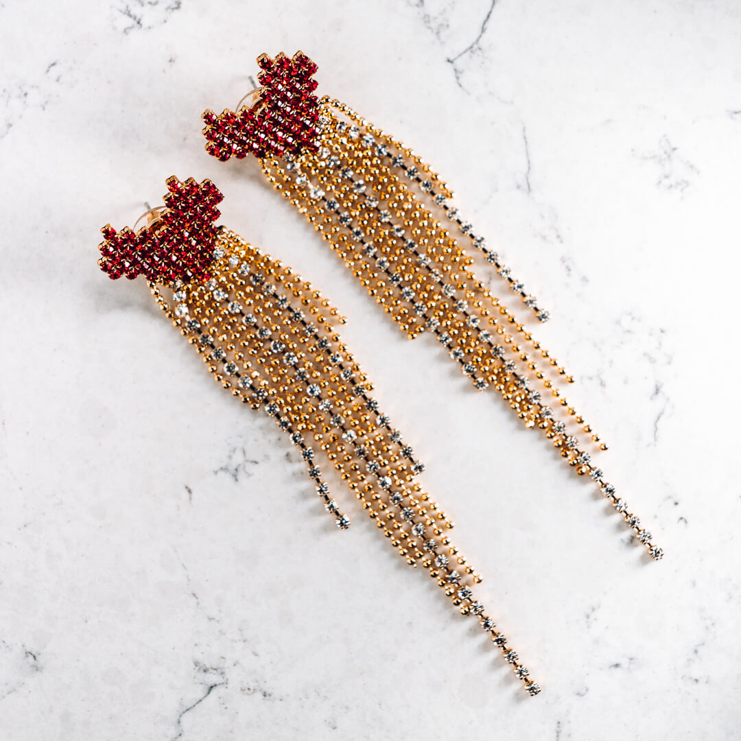 A pair of large earrings made up of a red heart with a gold tone and diamante tail.