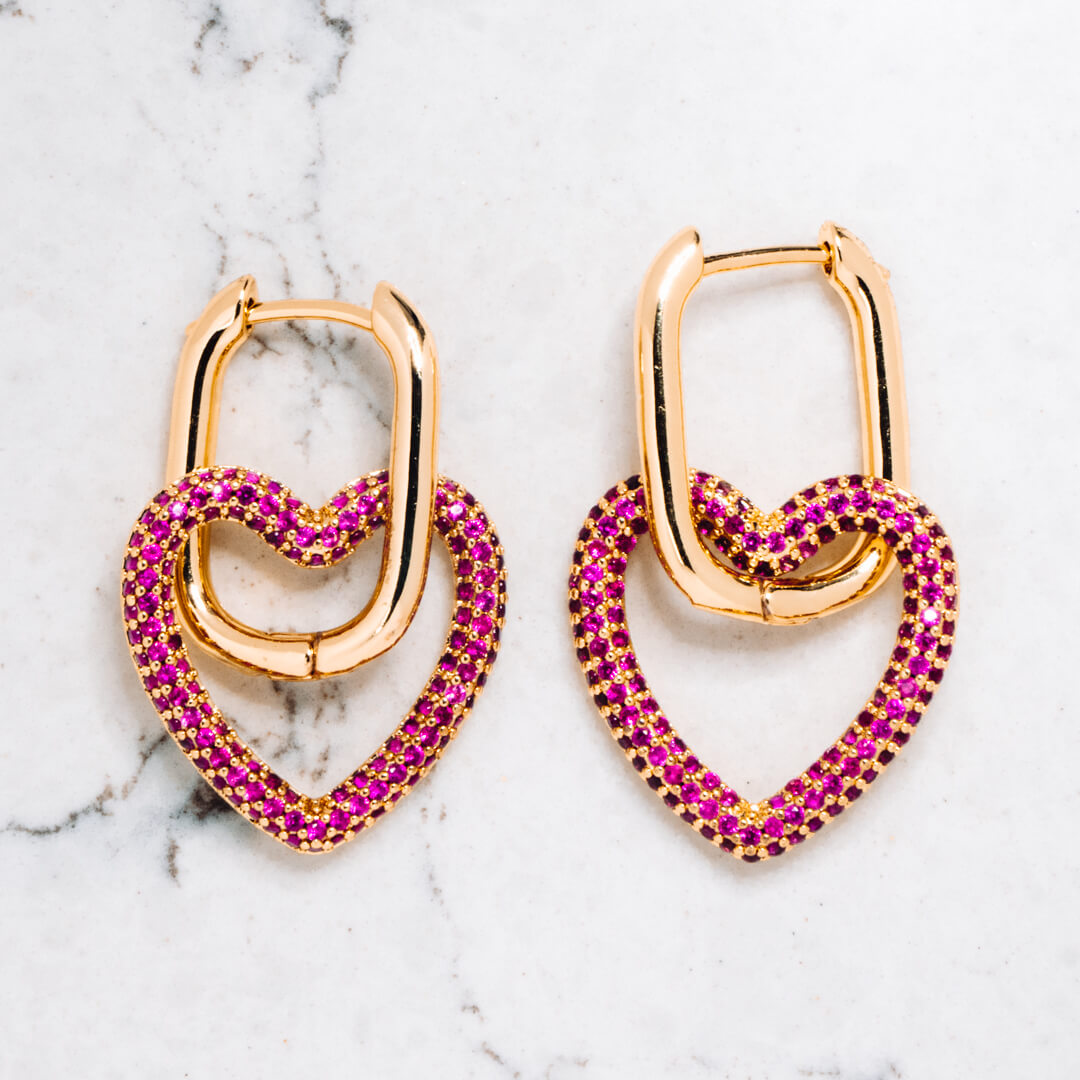 Gold tone earrings with heart shaped pendants in gold tone with pink coloured zircon stones.