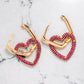 Gold tone earrings with heart shaped pendants in gold tone with pink coloured zircon stones.